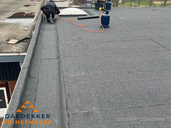Dakdekker repareert bitumen dakbedekking op groot plat dak in Prinsenbeek