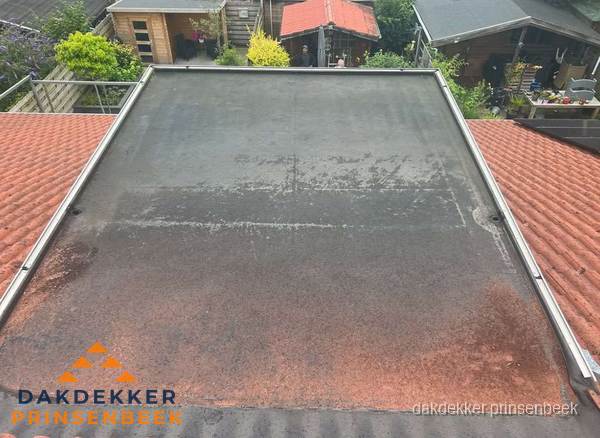 Verouderd plat dak met slijtage tussen schuine daken in Prinsenbeek